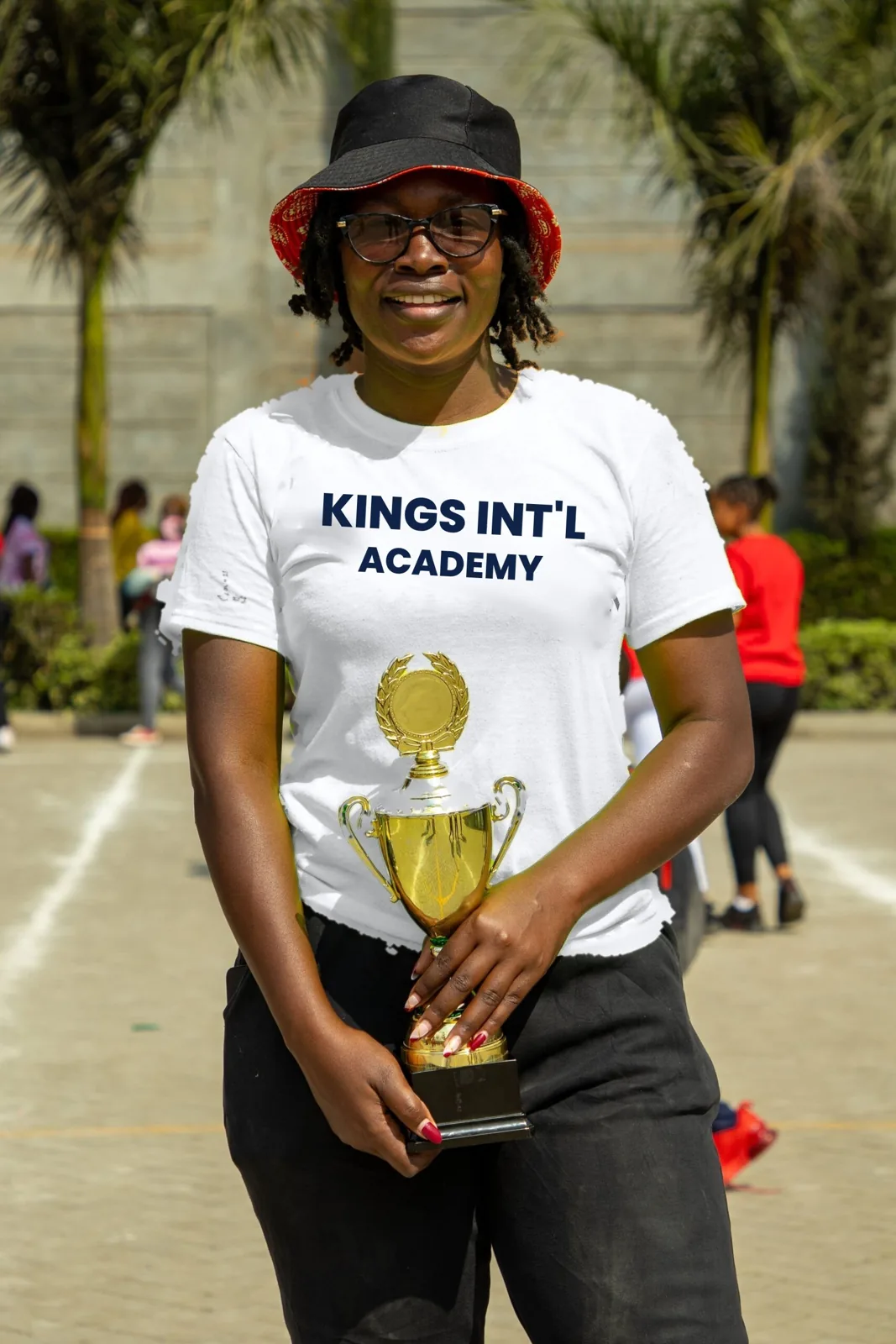 Kings International Academy staff member holding a Sports Day trophy, Fedha